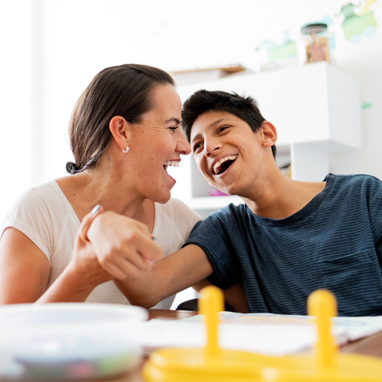 Mor og sønn som ler sammen ved bordet – glede og samspill i hverdagen.