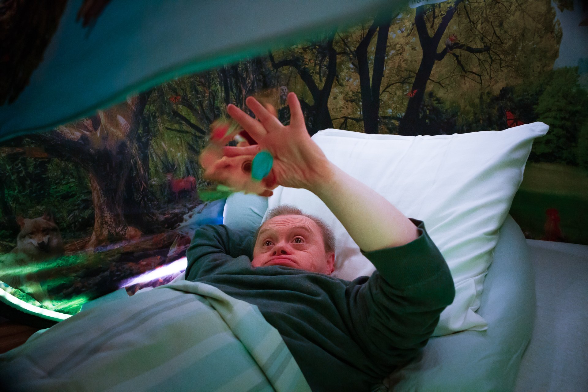 Person ligger i seng og ser opp mens Snoezle-telt med skogmotiv gir rolig belysning.