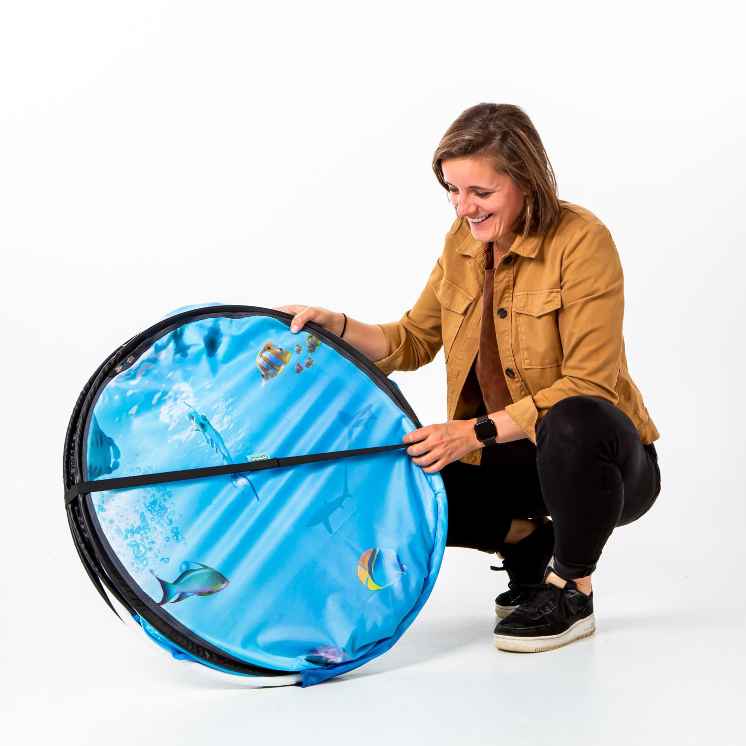 Kvinne smiler mens hun holder sammenbrettet Snoezle sansetelt med undervannsmotiv.