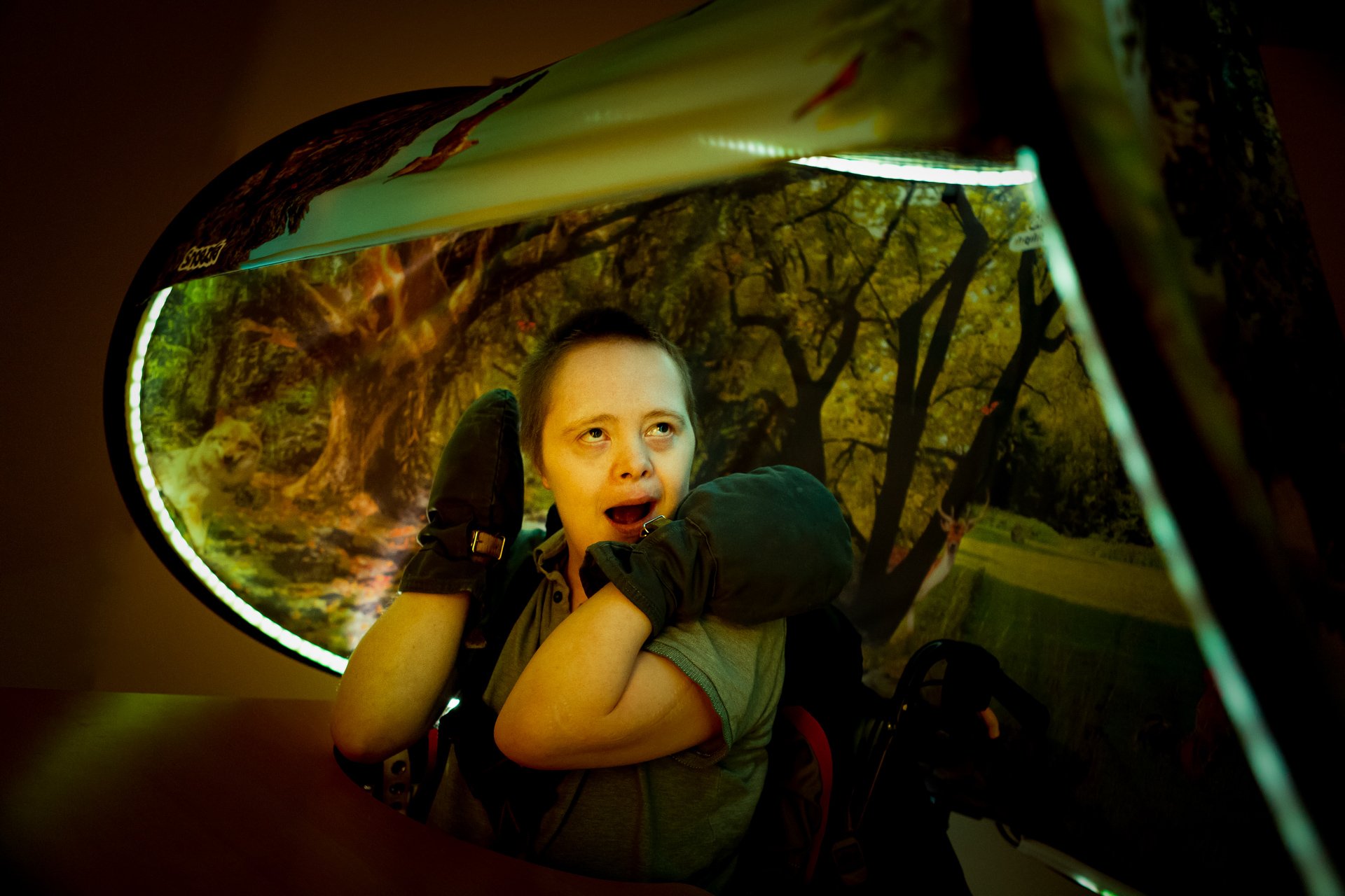 Person smiler og ser opp mens han sitter under Snoezle-telt med skogmotiv og grønt lys.